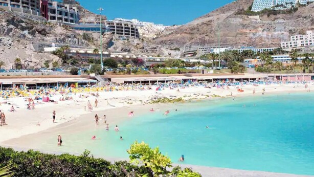 A beach resort with multiple swimming areas, a sandy beach, and buildings in the background.