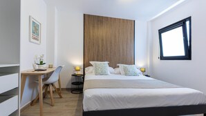 A modern bedroom with a bed, desk, chair, and a small table with a lamp.