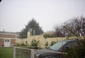 A fenced parking area with a car, a building with a brick facade, and a tree. - Hostel Viajeros (Puerto Madryn)