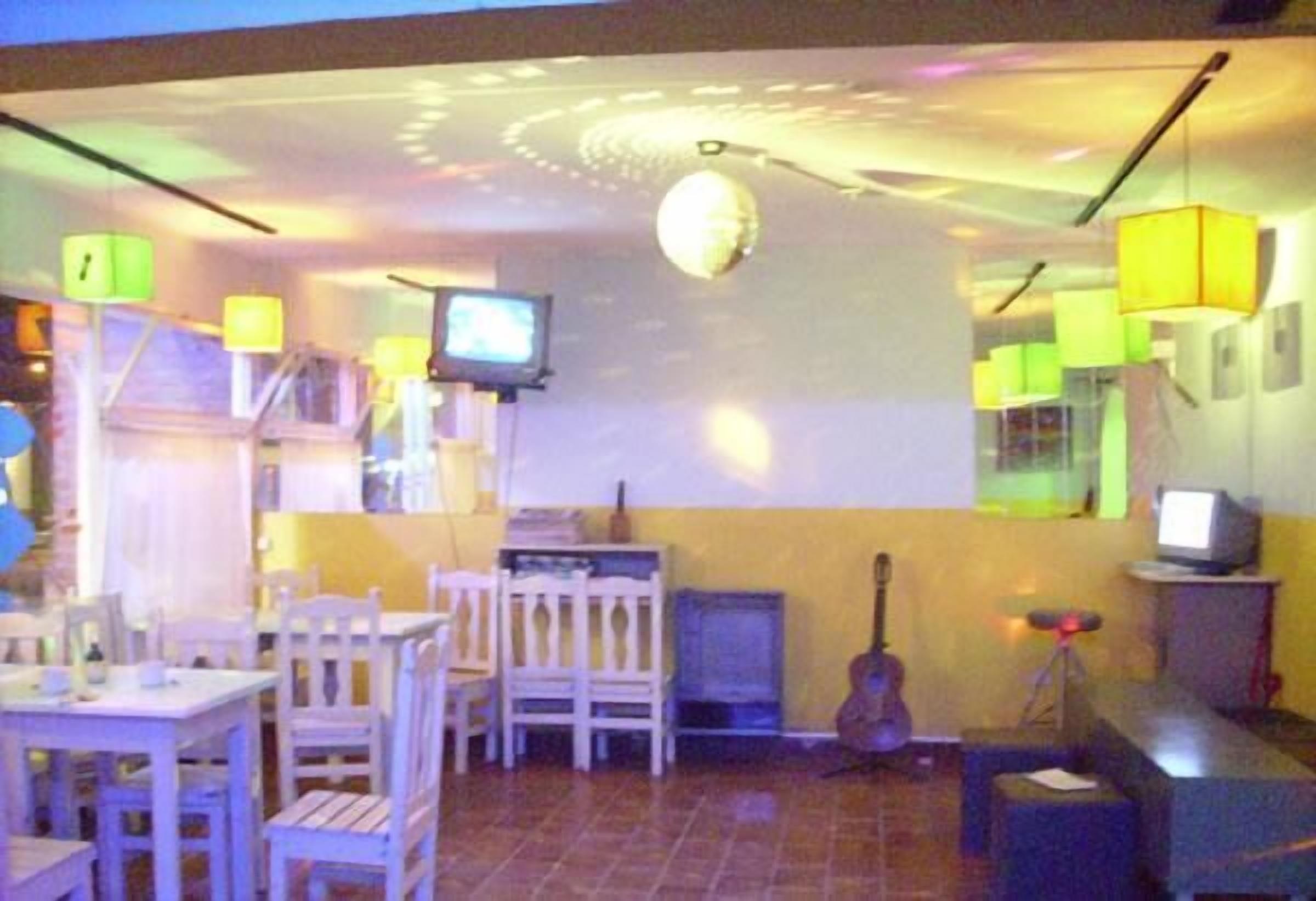 A room with a dining area, a television, a guitar, and a ceiling with a light fixture.