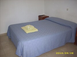 Una cama individual con una colcha azul y una toalla amarilla doblada encima.