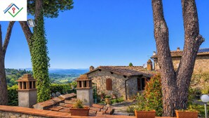 Un bâtiment en pierre avec un toit en tuiles, entouré d’arbres et de plantes en pot.