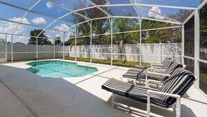 A covered outdoor swimming pool with lounge chairs and a white fence.