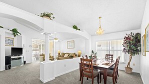 A spacious living area with a dining table, chairs, a sofa, and a kitchen in the background.