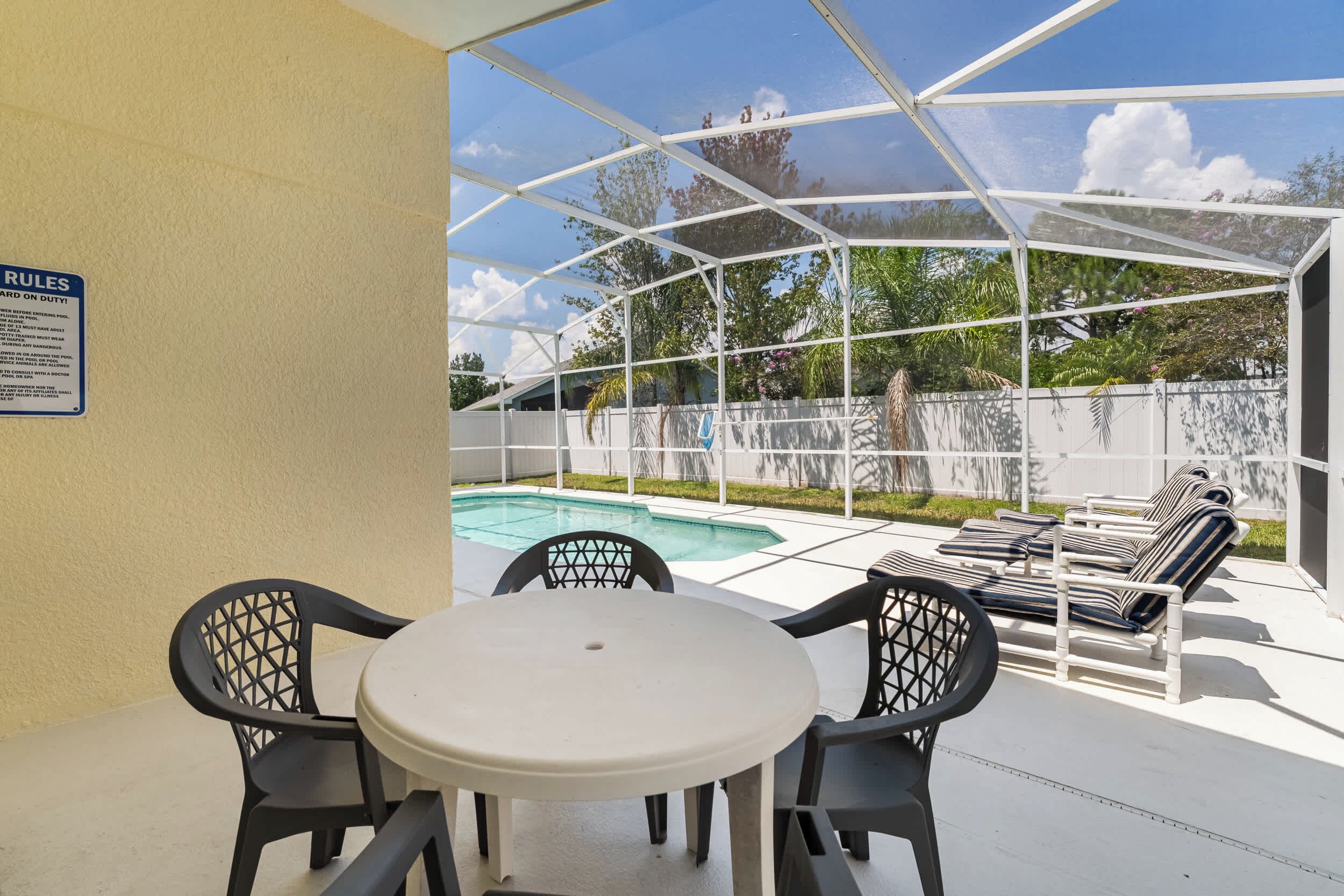 Ein überdachter Außenbereich mit Pool, Liegestühlen und einem Tisch mit Stühlen.