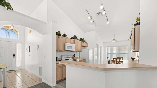 A modern kitchen with white cabinets, a central island, and built-in appliances. There is a dining area with a table and chairs.