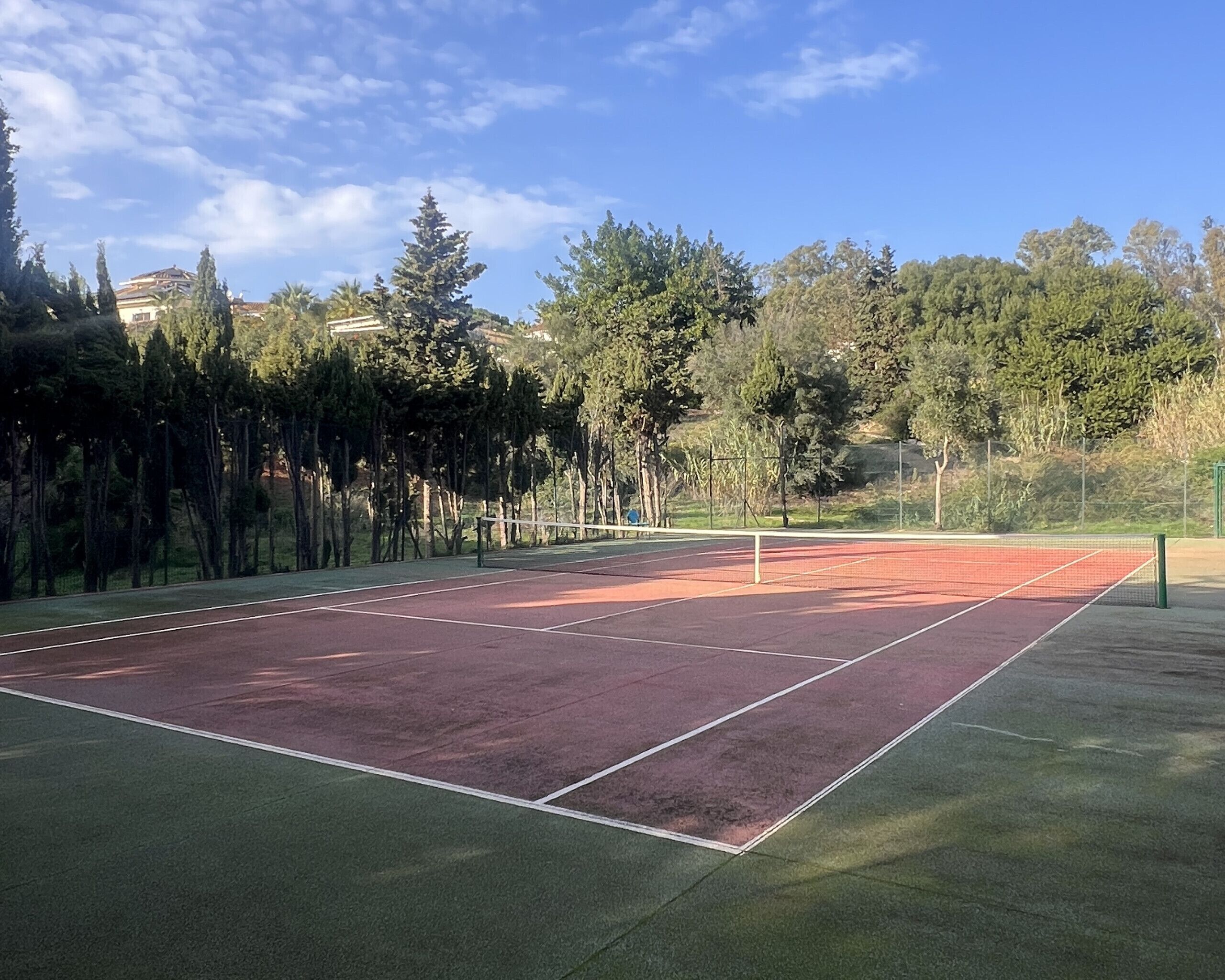 A tennis court surrounded by trees and a fence.