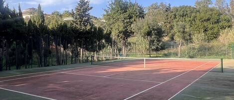 A tennis court surrounded by trees and a fence.