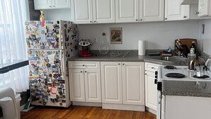 Une cuisine avec des meubles blancs, un réfrigérateur recouvert d’aimants, une cuisinière à gaz et un plan de travail sur lequel se trouvent divers objets.