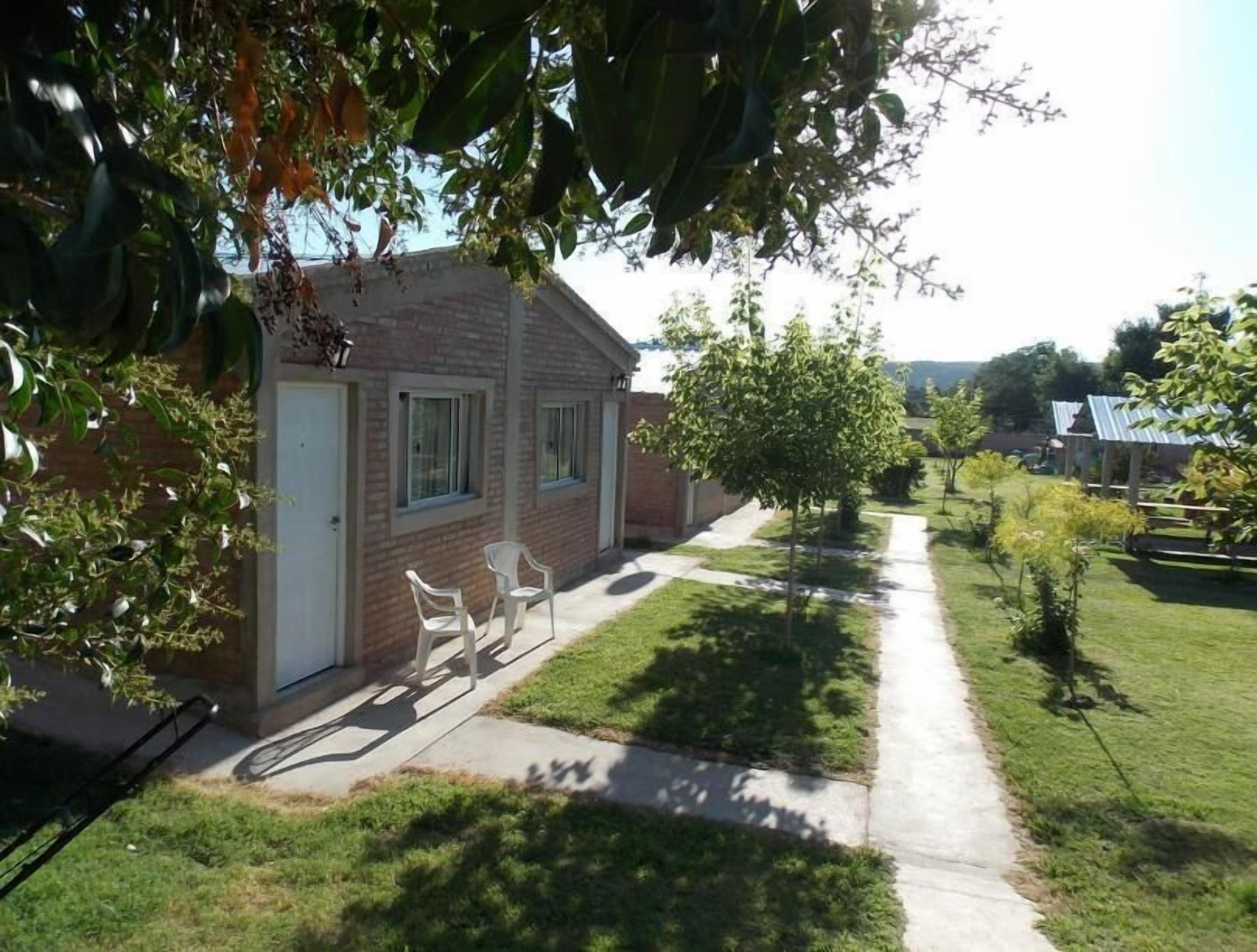 Una proprietà residenziale con una casa in mattoni, due sedie bianche all'esterno, un vialetto lastricato e un prato curato.