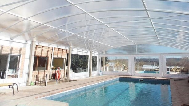 Ein überdachter Pool mit Glasdach, eine Terrassenfläche mit Sitzgelegenheiten und Blick auf die umliegende Landschaft.