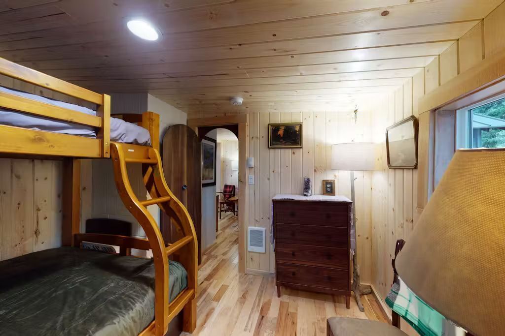 Ein Schlafraum mit Etagenbetten, einer Holzleiter, einem Schminktisch und einer Lampe.