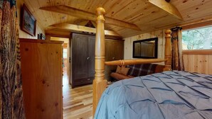 A wooden cabin interior with a four-poster bed, a wardrobe, and a mirror on the wall.