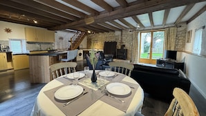 Un coin repas avec une table ronde dressée pour quatre personnes, une cheminée en pierre et une vue sur l’extérieur grâce à une grande fenêtre.