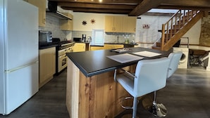 Une cuisine avec des poutres en bois, un îlot central et un tabouret de bar.