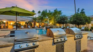 An outdoor pool area with two barbecue grills, lounge chairs, and a covered seating area. - Landing | Chic 1BD, Gym, Pool (Phoenix)