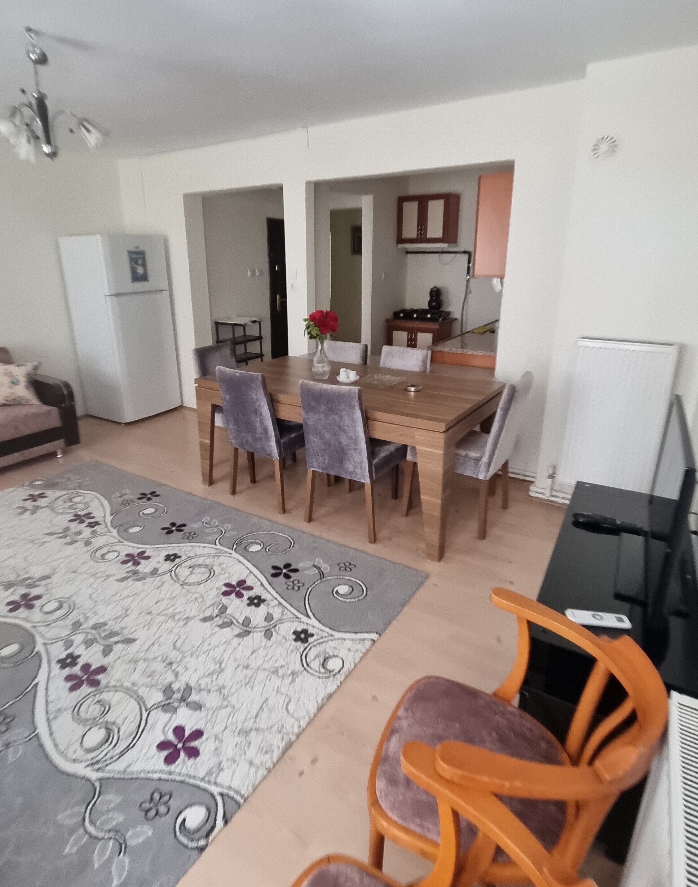 Un comedor con una mesa y sillas de madera, un refrigerador, una zona de cocina y un tapete estampado.