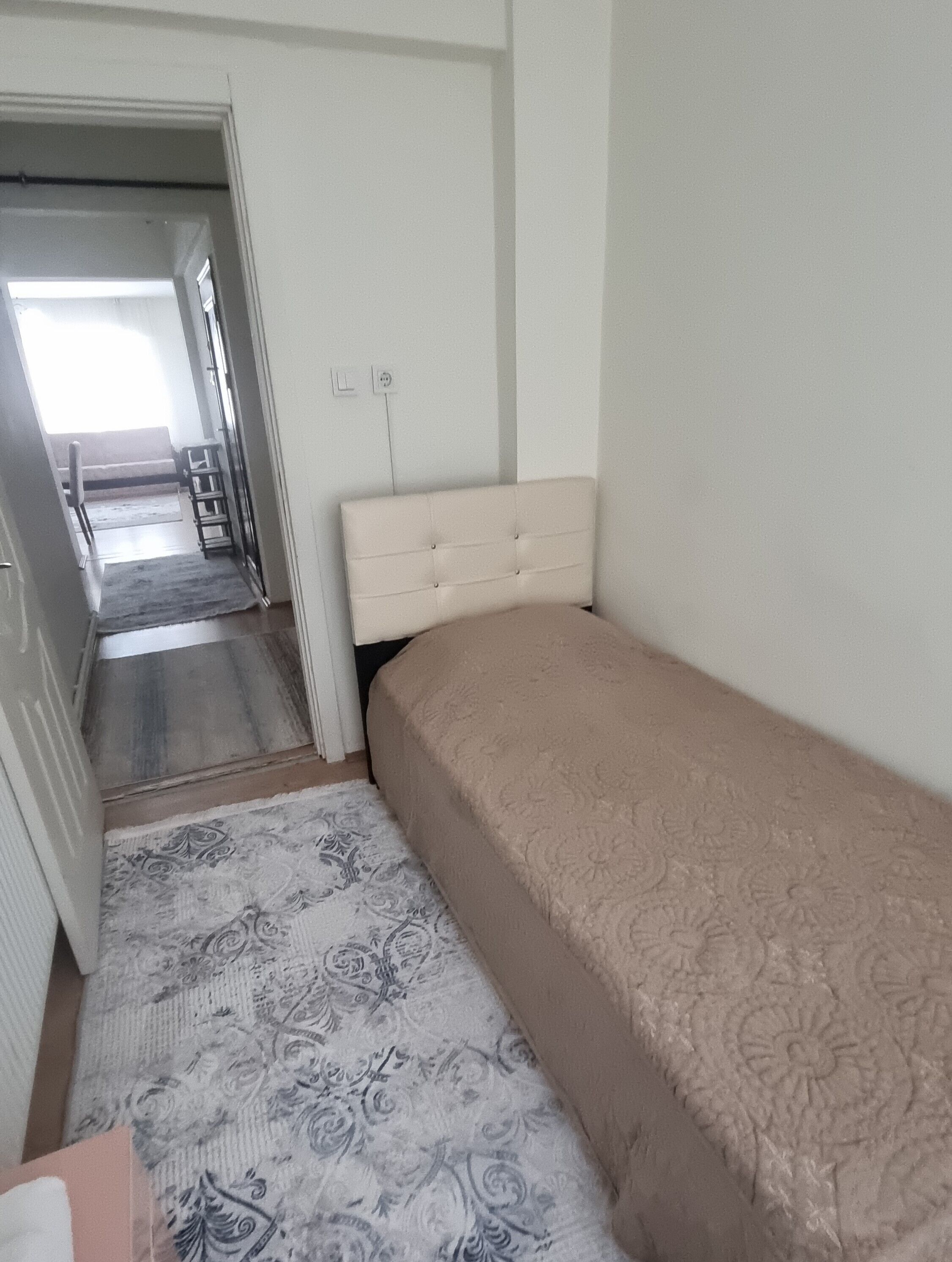 A bedroom with a single bed, a patterned rug, and a doorway leading to another room.