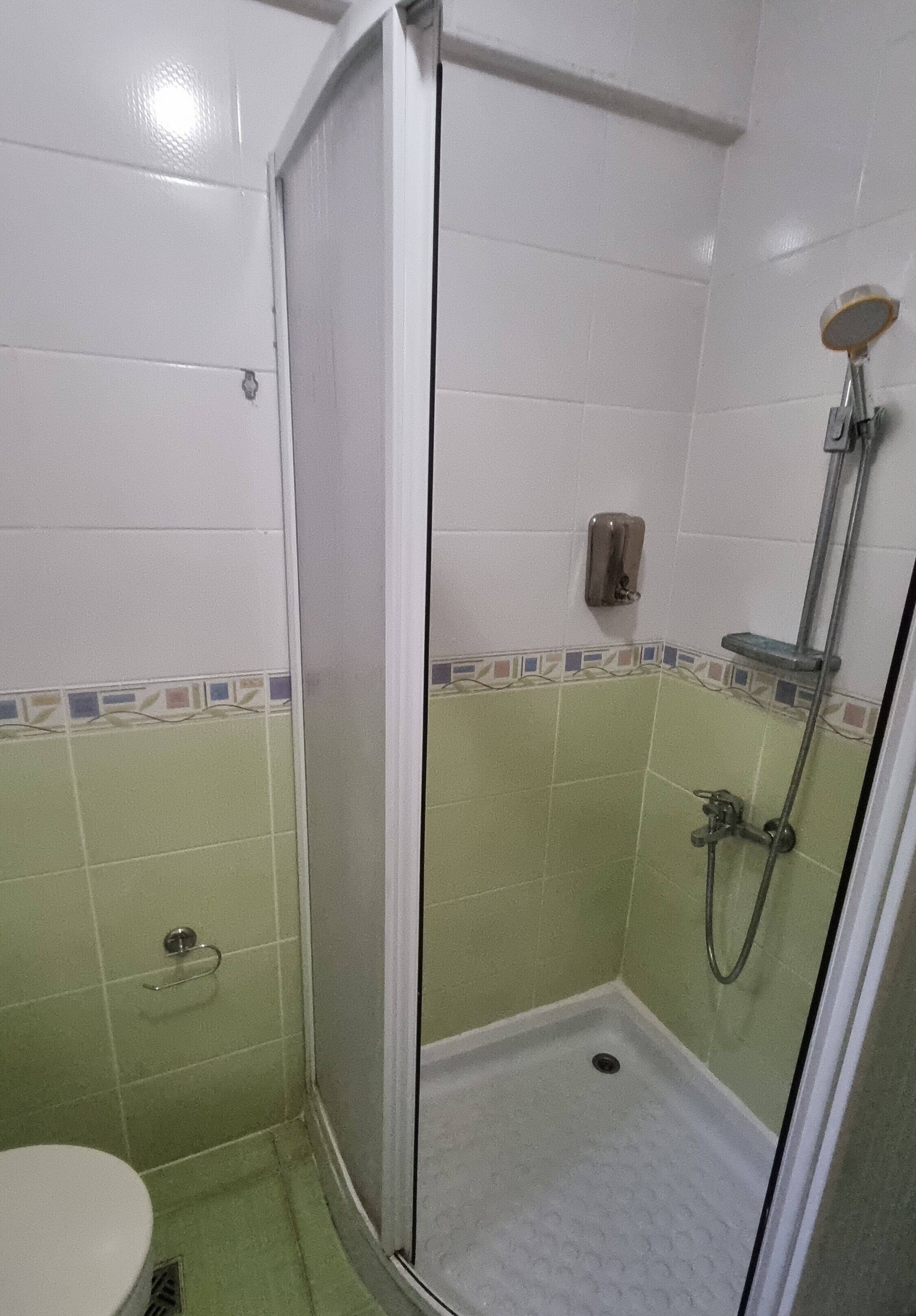 A small, enclosed shower area with a glass door, a handheld showerhead, and a soap dispenser on the wall.