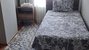 A bedroom with a bed, a nightstand, a patterned rug, and a window with curtains.