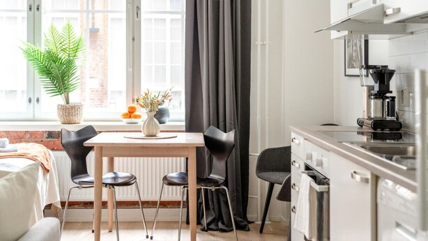 A modern kitchen with a coffee machine, a dining area with a table and chairs, a potted plant, and a view of the outside through large windows. - Come in! `Värjäri` Stunning stud (Tampere)
