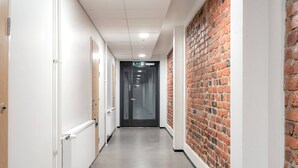 A corridor with white walls, a brick accent wall, and a door at the end. - Come in! `Värjäri` Stunning stud (Tampere)