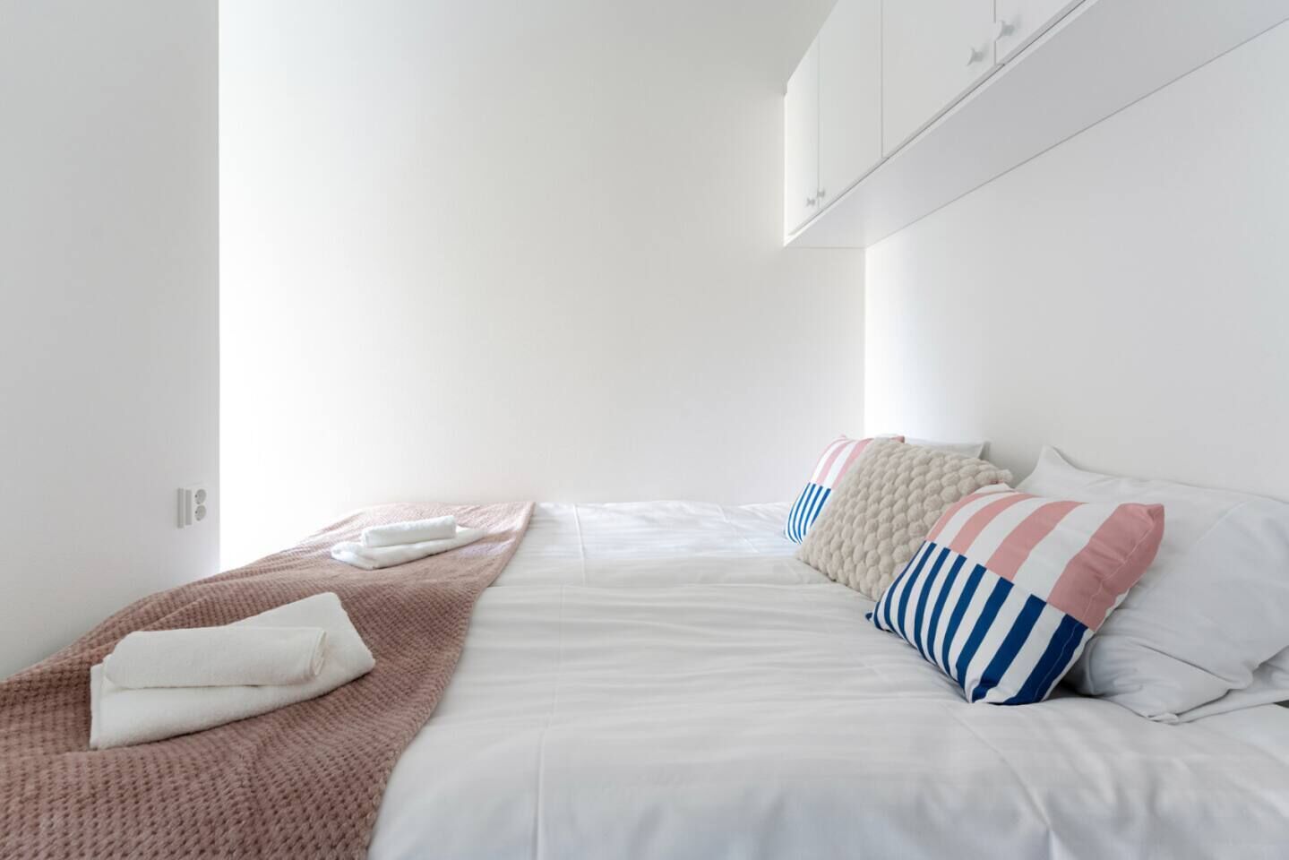 A minimalist hotel room with a bed, pillows, a blanket, and a towel.