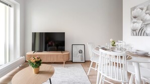 A modern living room with a flat-screen TV, a dining area with white chairs, a round table, and a large window. - Come in! `Vapari 2` Astonishing studio in stadium! (Tampere)
