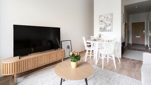 A modern living room with a flat-screen TV, a wooden entertainment unit, a dining area with white chairs, and a small round table with a plant. - Come in! `Vapari 2` Astonishing studio in stadium! (Tampere)