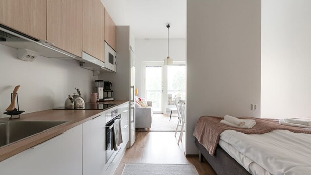 A modern kitchen with wooden cabinets, a built-in oven, and a coffee machine. - Come in! `Vapari 2` Astonishing studio in stadium! (Tampere)
