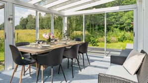 Un invernadero con una mesa de comedor dispuesta para seis personas, rodeada de sillas y un sofá de mimbre.