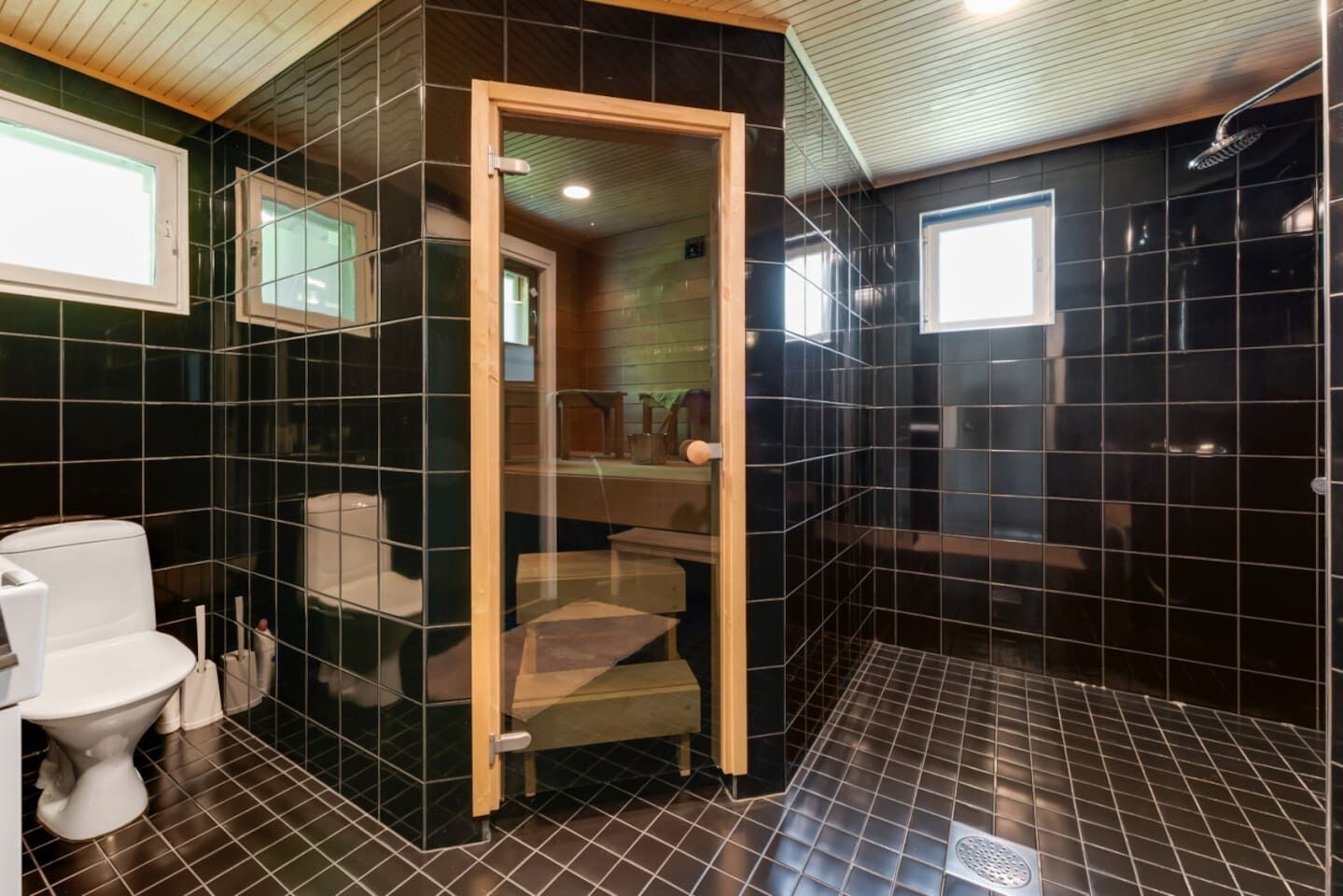 A bathroom with black tiled walls, a wooden door, a white toilet, and a shower area.
