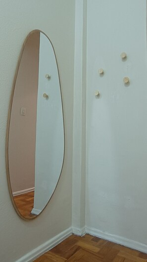 A corner of a room with a white wall, a wooden floor, and a large oval mirror with a wooden frame. - Few steps from Ipanema & Arpoador Beaches (Ipanema)