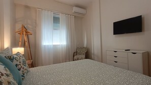 Habitación de hotel con una cama, una silla, un escritorio, un televisor y un equipo de aire acondicionado.