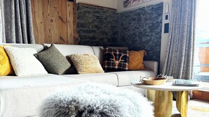 A cozy living room with a wooden ceiling, a stone wall, and a sofa with various cushions.