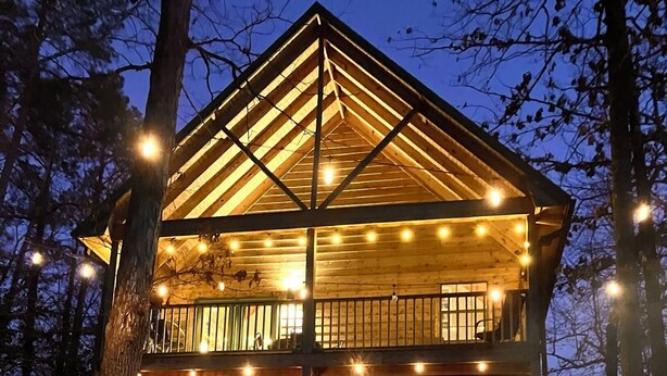 A two-story wooden cabin with a balcony, outdoor seating, and a fire pit.