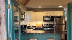 A kitchen with a central island, two bar stools, and a stainless steel refrigerator.