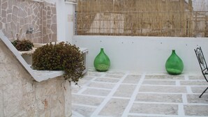 Una terraza en la azotea con paredes de piedra, barandilla blanca y dos jarrones verdes.