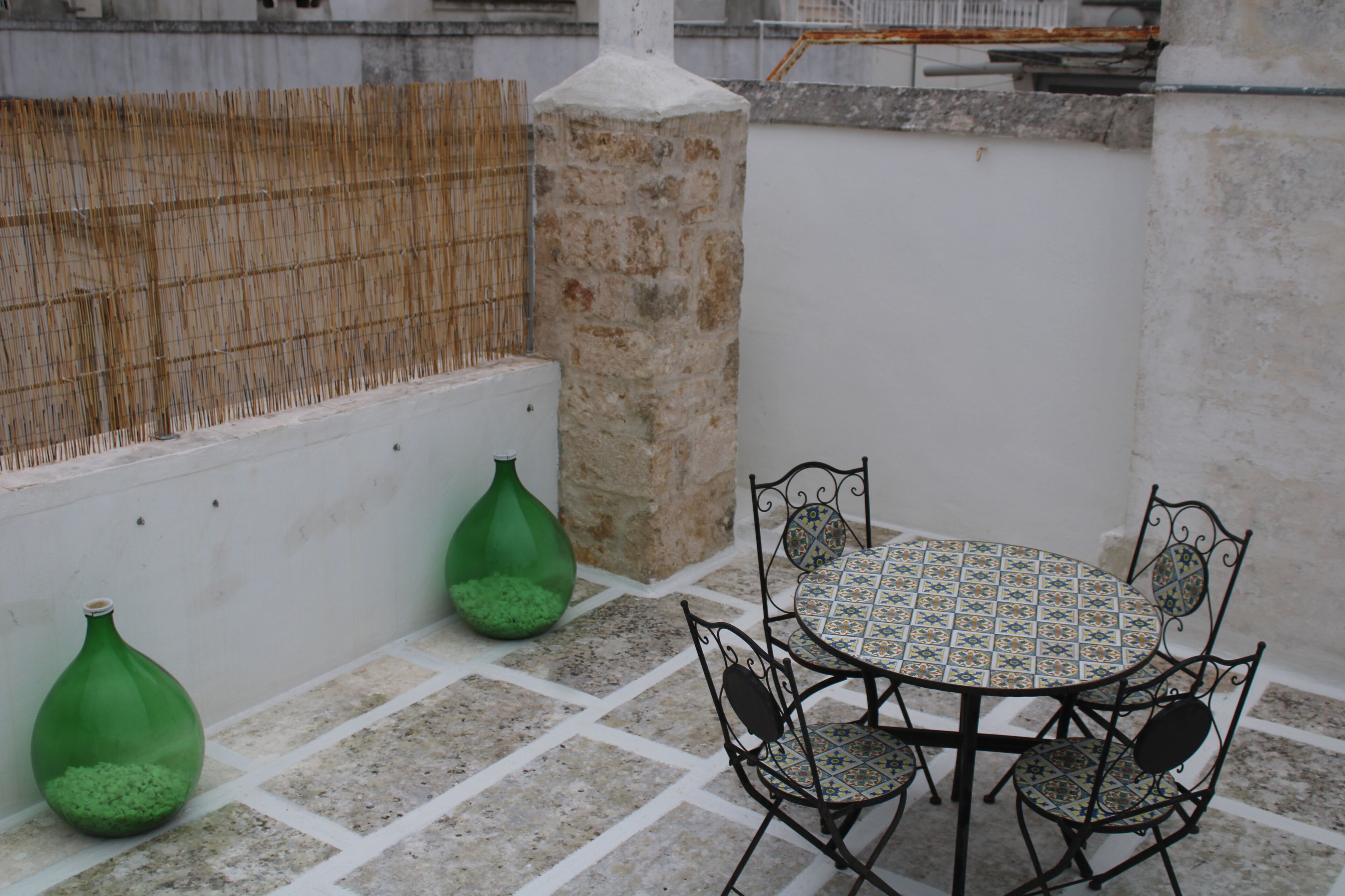 A small outdoor patio with a round table and four chairs, a stone pillar, and two green vases.