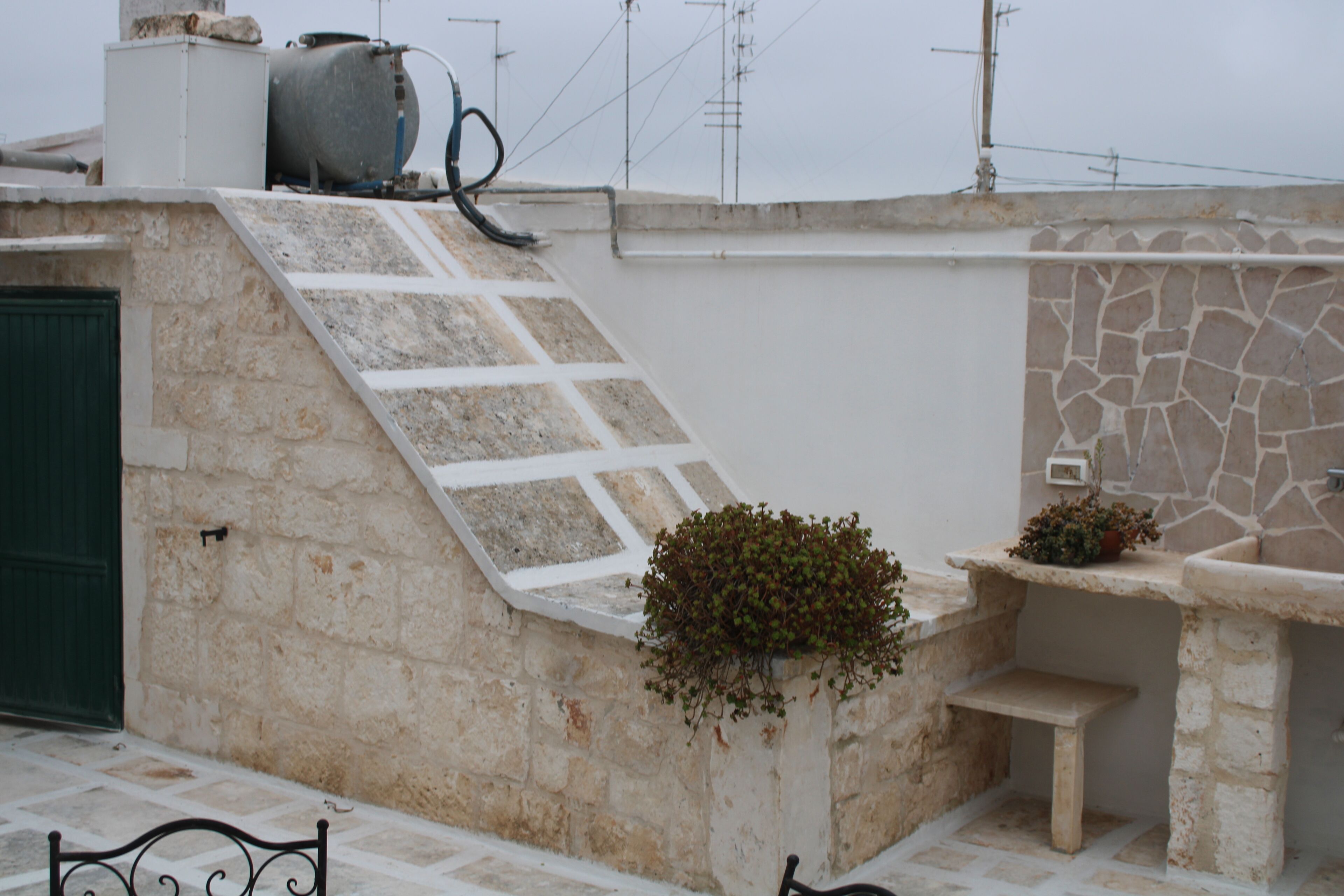 Une façade en pierre, un escalier en métal, une porte verte et un petit banc.