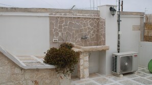 Una terraza en la azotea con un muro de piedra, un lavamanos pequeño y un equipo de aire acondicionado.