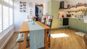 A cozy kitchen with a dining area, featuring a wooden table, chairs, and a view of the adjacent dining room. - The Canalside Cottage (Derby)