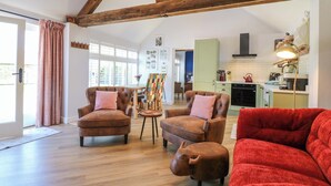 A spacious living room with wooden beams, two brown leather armchairs, a red sofa, and a pig-shaped ottoman. A painting easel and a dining table are in the background. - The Canalside Cottage (Derby)