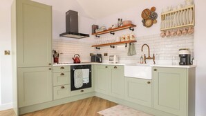 A kitchen with light green cabinets, a wooden floor, a built-in oven, a sink, and various kitchen appliances. - The Canalside Cottage (Derby)