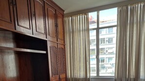 A room with a bed, wooden wardrobe, and a window with curtains. - Charming apartment in enjoyable Flamengo Rio de Janeiro near Park Aterro (Flamengo Rio de Janeiro)