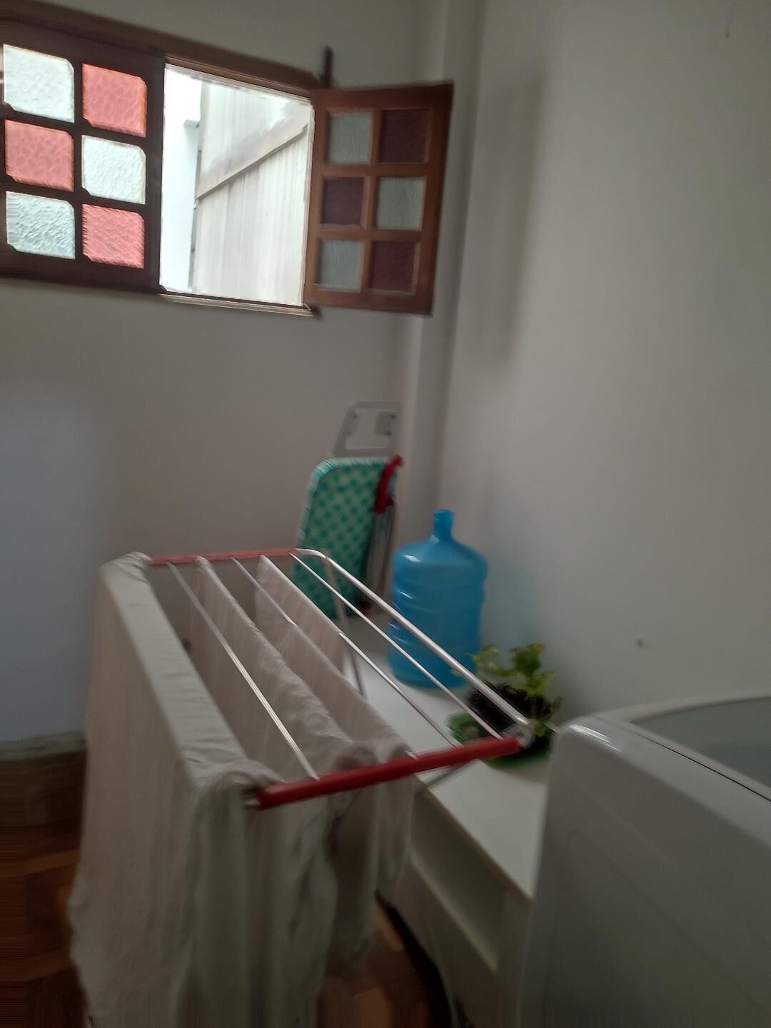 A laundry area with a drying rack, a large blue water dispenser, and a window with a view of the outside.
