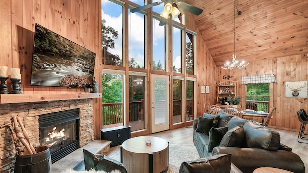 A cozy cabin interior with a fireplace, comfortable seating, and large windows offering a view of the outdoors. - Mountainside retreat in the Smokies!  6 miles to The Island. Sleeps 8. (Sevierville)