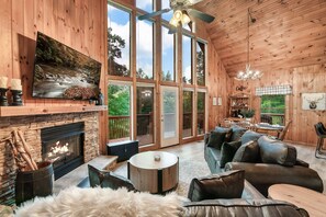 Interior acogedor de una cabaña con chimenea, asientos cómodos y ventanas amplias que ofrecen vistas al exterior.