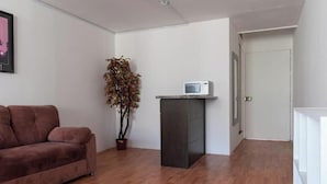 A room with a brown sofa, a potted plant, a microwave on a cabinet, and a white door.