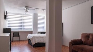 A bedroom with a bed, a desk, a chair, a brown sofa, and a ceiling fan.
